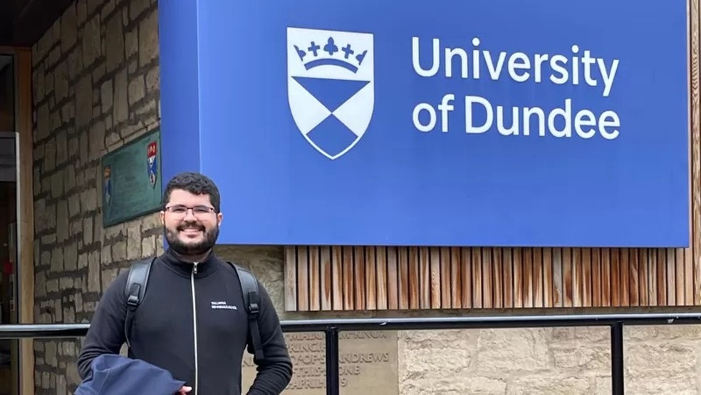 Dener Silva Miranda em frente ao logotipo da Universidade de Dundee, na Escócia, onde ele estudou pelo programa Ciência Sem Fronteiras — Foto: ARQUIVO PESSOAL via BBC