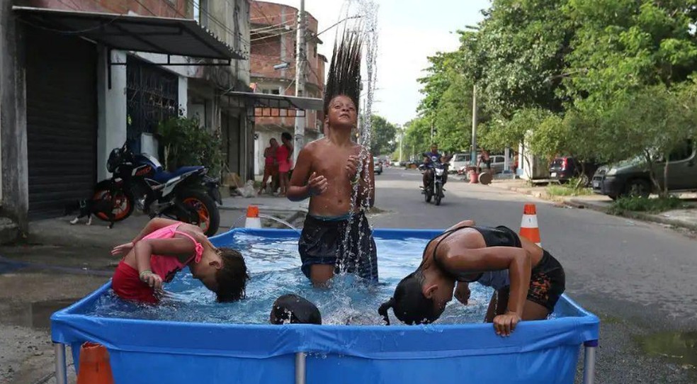 Crianças se refrescam na água para aliviar o calor intenso durante uma onda de calor registrada no Rio de Janeiro, em 2023 — Foto: Tânia Rêgo/Agência Brasil via BBC News