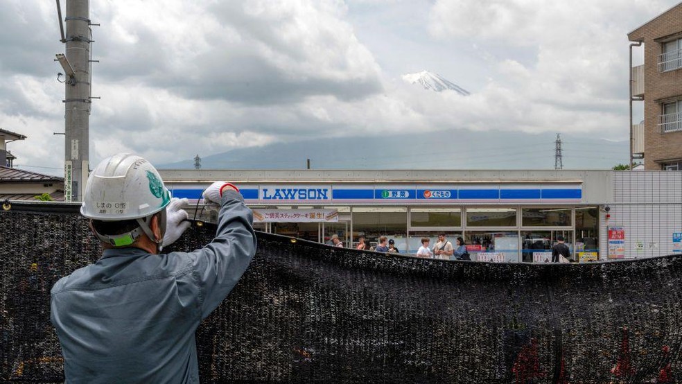 A famosa imagem na cidade de Fujikawaguchiko mostra uma loja de conveniência em primeiro plano, com a vista mais conhecida do monte Fuji, no Japão, erguendo-se atrás dela — Foto: BBC News fonte