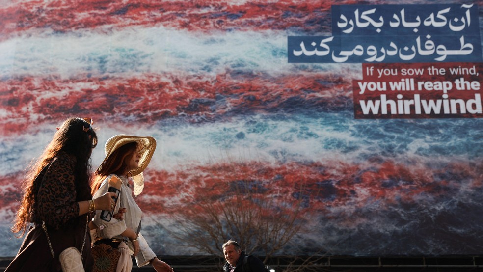 Iranianos caminham em outdoor com mensagem anti-EUA em Teerã: "Se você semear o vento, colherá o vendaval" — Foto: BBC News fonte