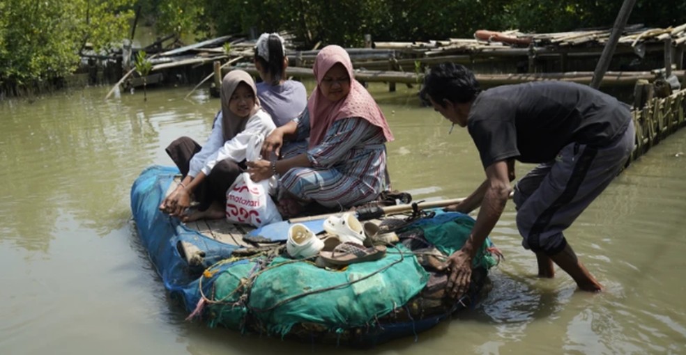 Os filhos de Ningsih usam uma balsa improvisada para ir à escola. A balsa é feita com restos de isopor e um colchão velho — Foto: Ayomi Amindoni/BBC