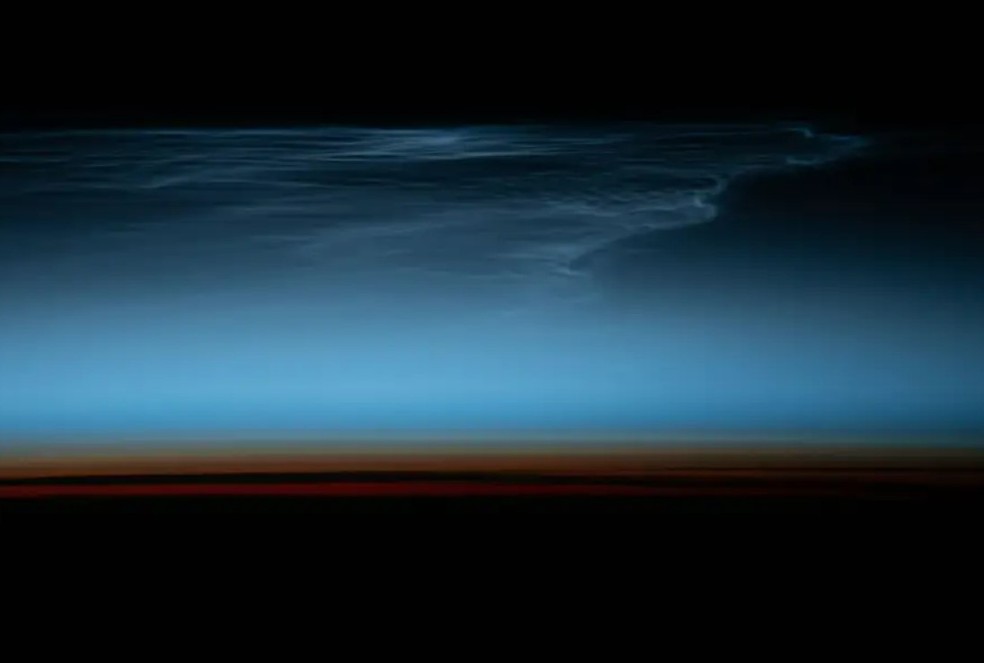 Nuvens noctilucentes tênues na atmosfera superior da Terra são iluminadas pela luz do sol logo após o pôr do sol acima do Oceano Pacífico Sul — Foto: Nasa