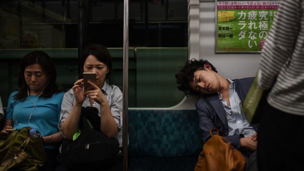 Não é incomum encontrar assalariados exaustos dormindo no metrô de Tóquio — Foto: BBC News fonte