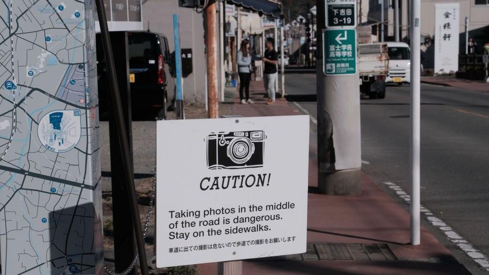 'Cuidado! Tirar fotos no meio da rua é perigoso. Permaneça na calçada', diz o cartaz em inglês e japonês em Fujiyoshida, no Japão — Foto: BBC News fonte
