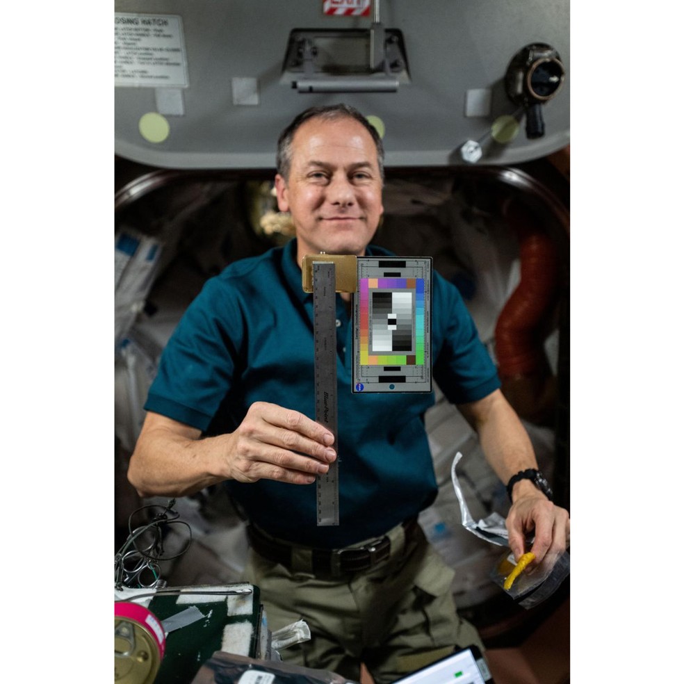 Thomas Marshburn posa para foto com cartela de cores e uma régua a bordo da ISS.  — Foto: NASA