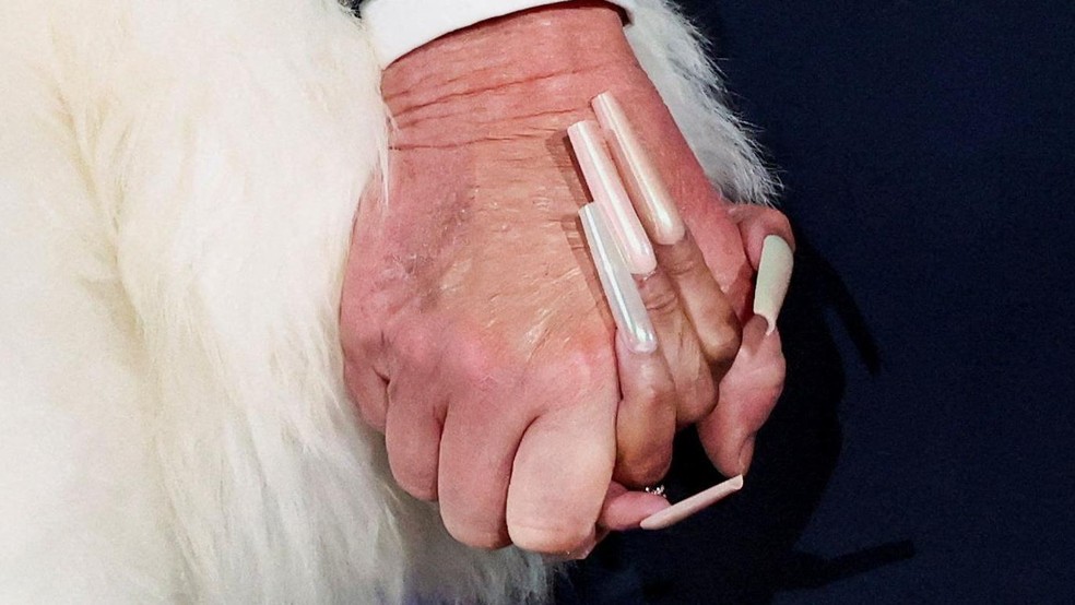 Minaj, com suas longas unhas características, de mãos dadas no palco com Donald Trump — Foto: BBC News fonte