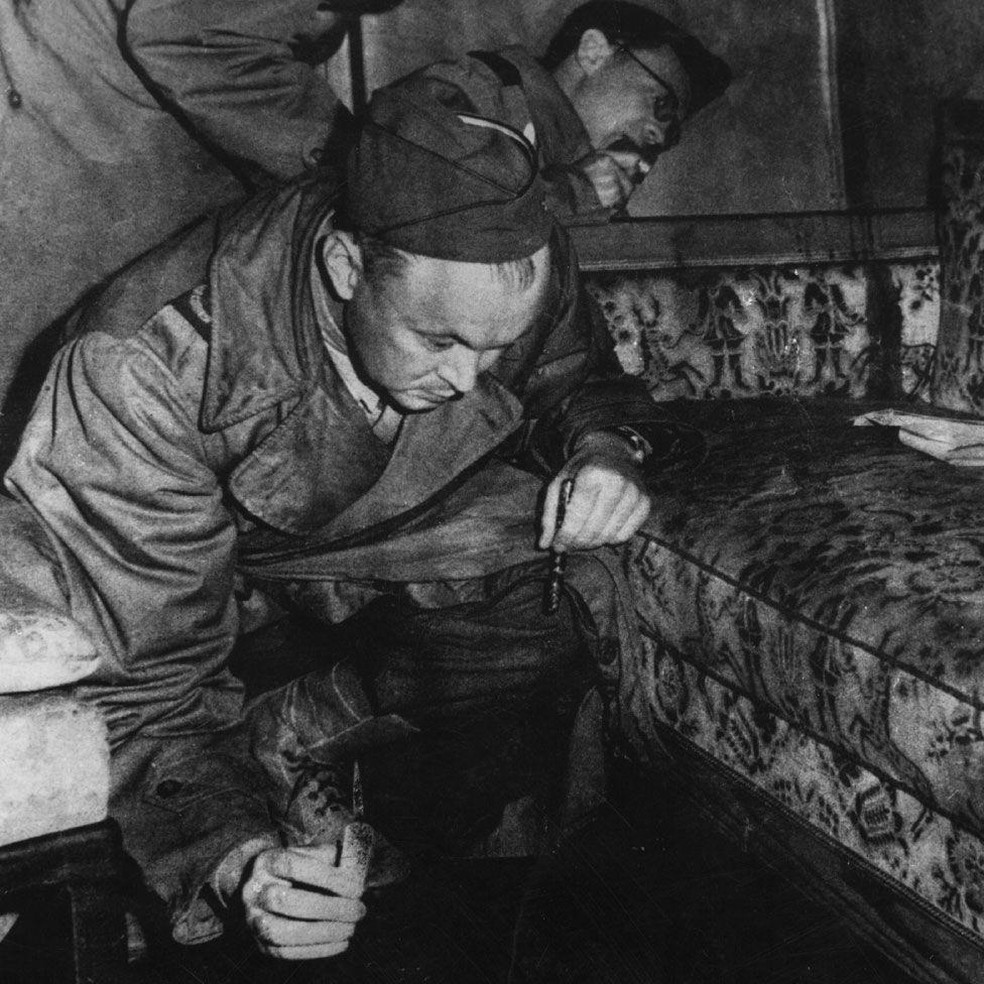 Jornalistas de guerra examinam o sofá dentro do bunker de Hitler em 1945 — acredita-se que a mancha no braço da cadeira é sangue — Foto: BBC News fonte