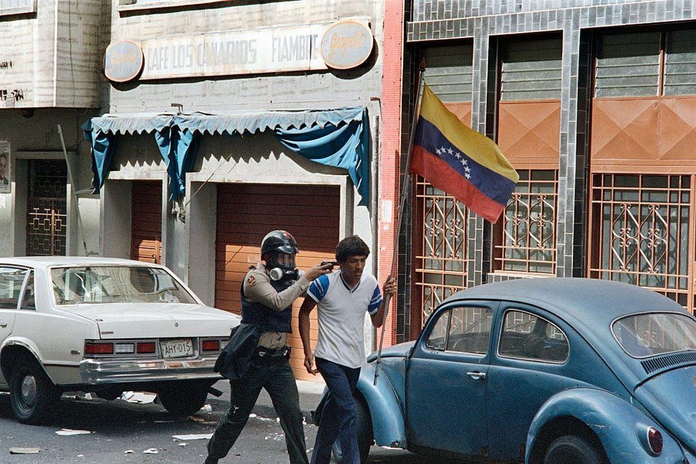 Manifestante carregando uma bandeira venezuelana é preso por um membro da Guarda Nacional em 27 de fevereiro de 1989, durante o segundo dia de protestos contra medidas do governo — Foto: BBC News fonte