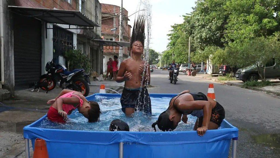Crianças se refrescam na água para aliviar o calor intenso durante uma onda de calor registrada no Rio de Janeiro, em 2023 — Foto: BBC News fonte